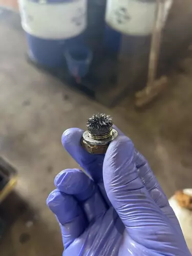 Close-up of oil drain plug with metal debris and contamination from pump during servicing of a Nilfisk SH Truck Booster, indicating wear inside the pump.